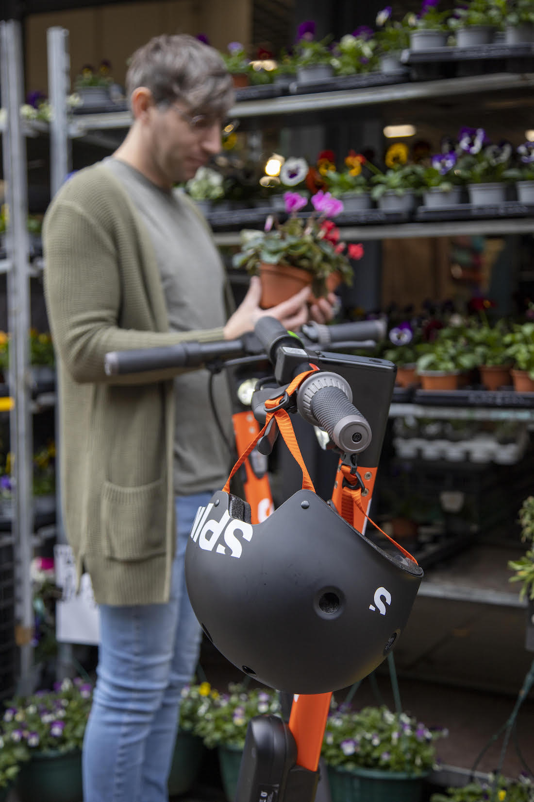 a scooter with a helmet in front of a man shopping for flowers.